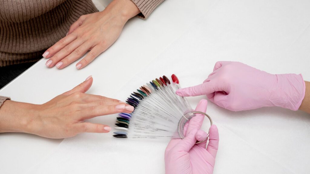Manicurista mostrando un muestrario de colores de esmaltes a una clienta en salón.