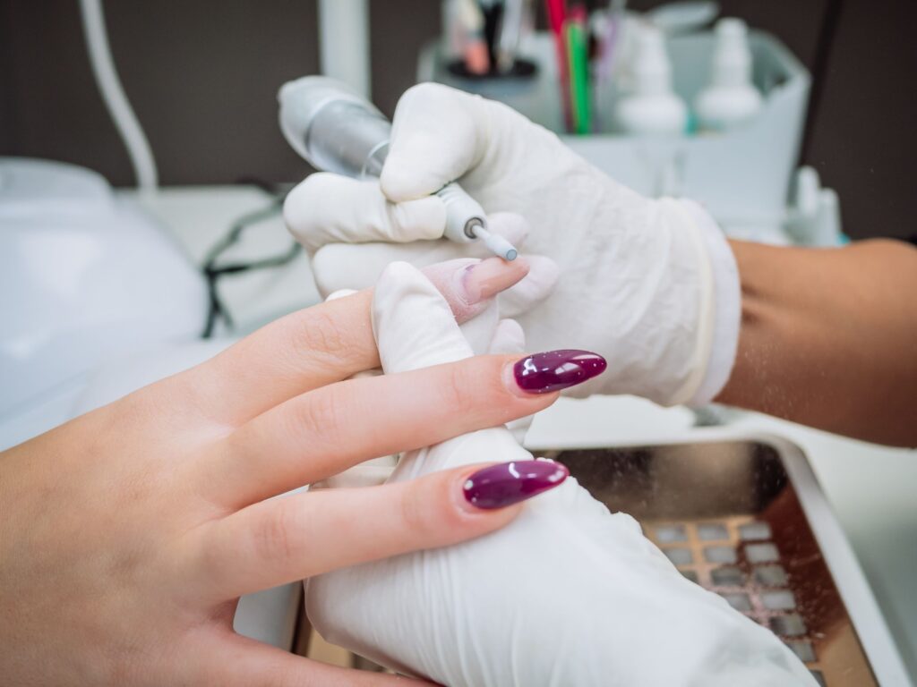 Manicurista utilizando torno micromotor para retirar cutícula y preparar la superficie de la uña.