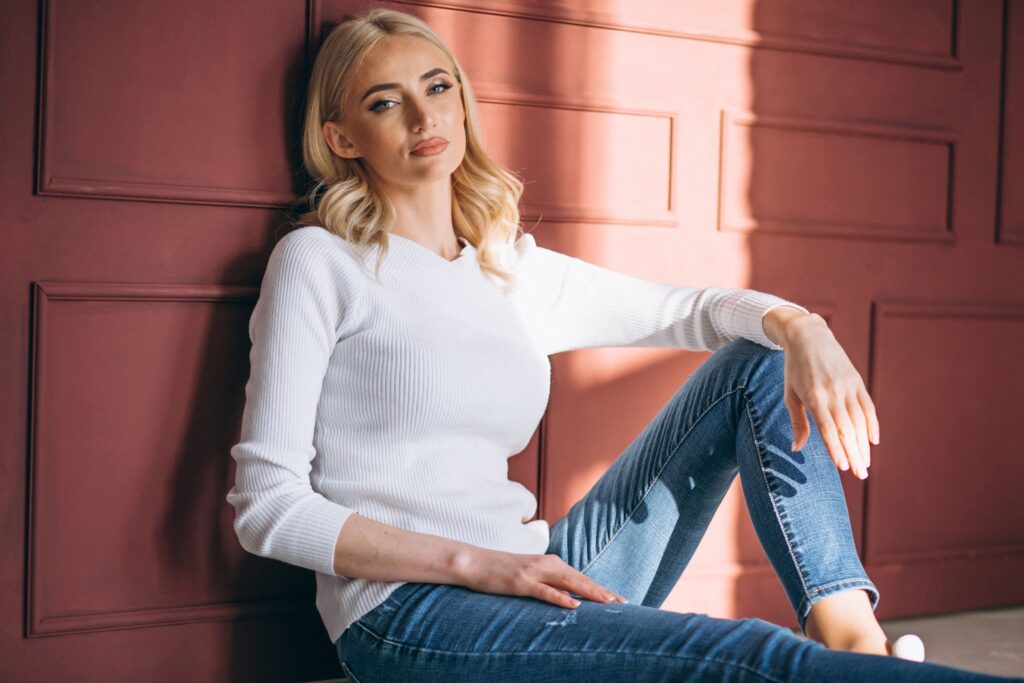 Mujer sentada con jersey de algodón blanco de cuello redondo y vaqueros azules.